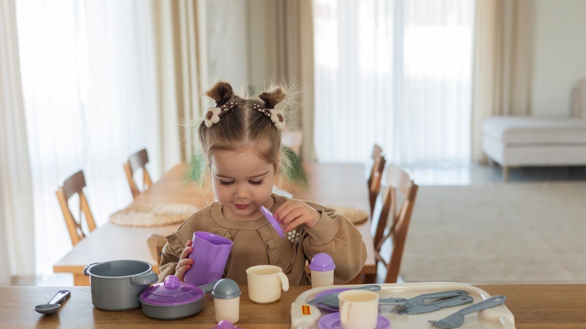 A young girl playing with a colorful toy tea set on a wooden table indoors.