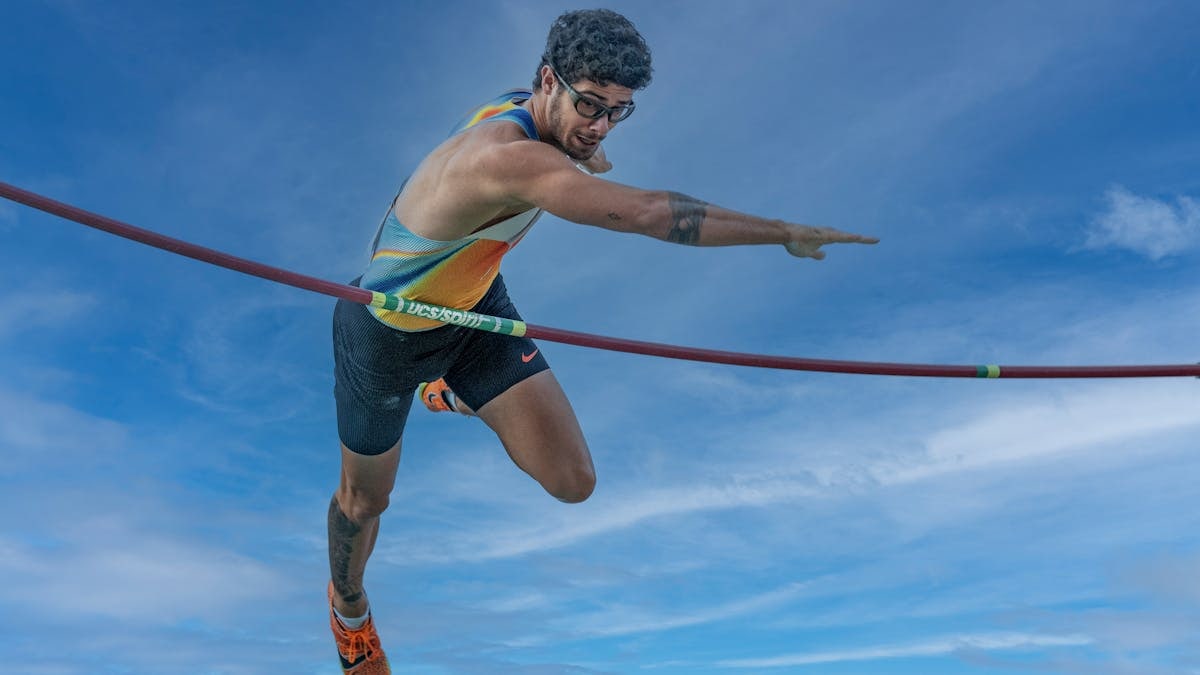 High-energy capture of a pole vaulter in action against a vibrant sky.